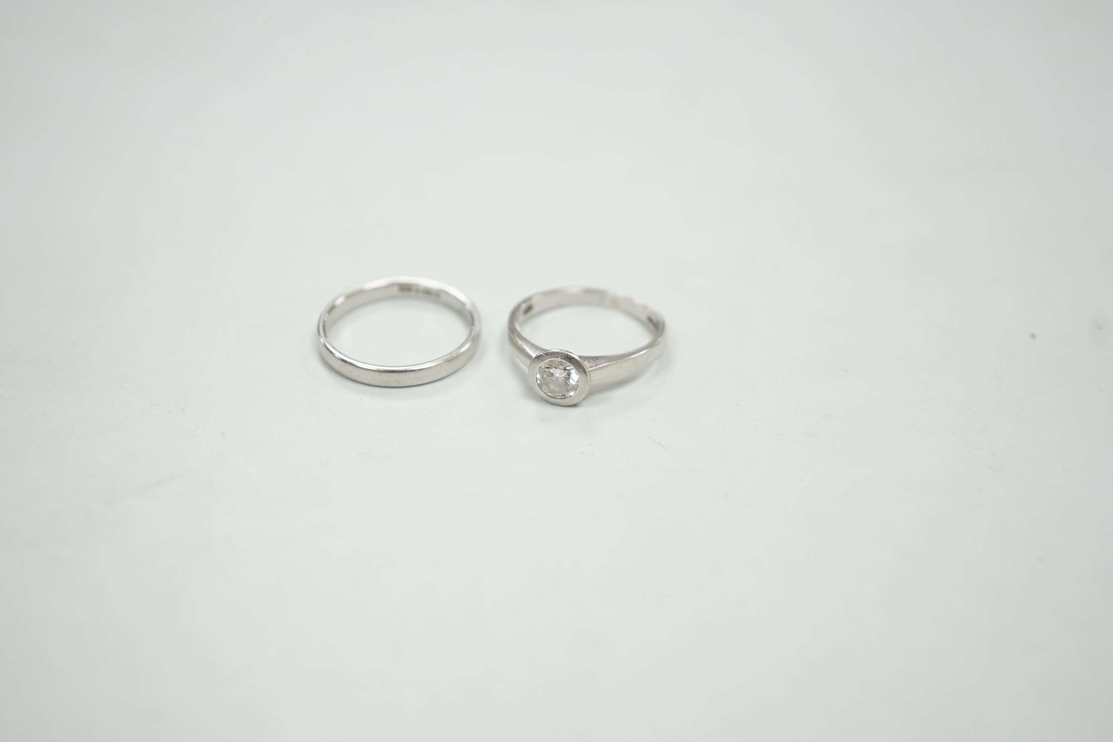 A modern platinum and collet set solitaire diamond ring, size M, gross weight 4.9 grams, together with a modern platinum wedding band, size N, 3.8 grams.